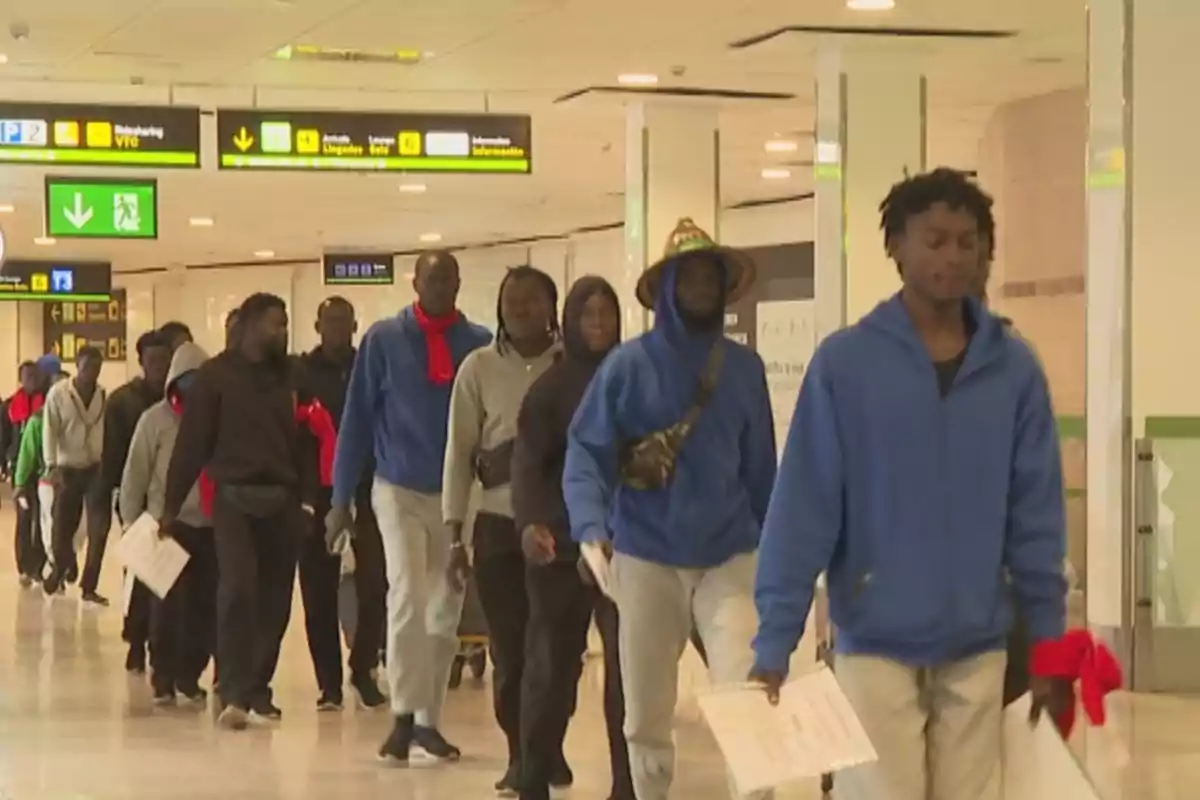 Un grupo de inmigrantes caminando en fila dentro de un aeropuerto.