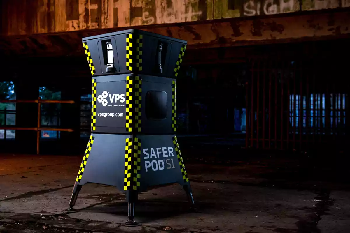 Una estructura de seguridad negra con detalles amarillos y negros ubicada en un entorno industrial oscuro con el logotipo de VPS y la inscripción "SAFER POD S1".