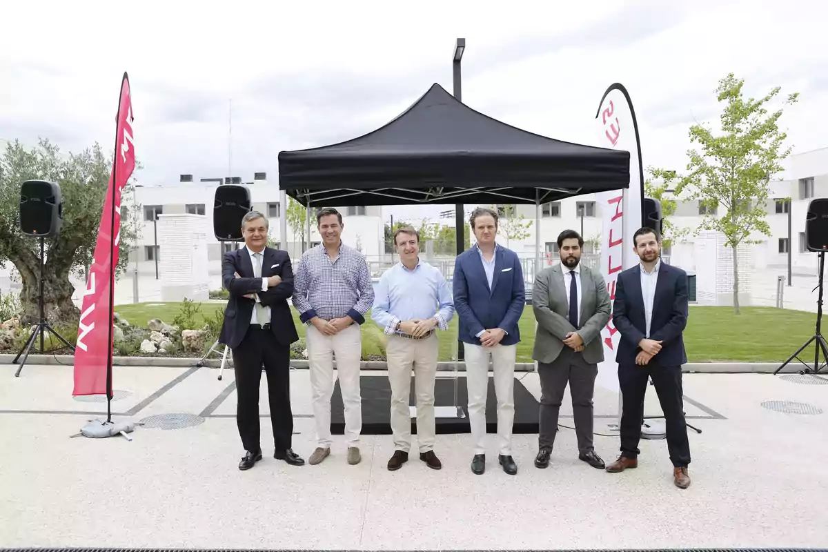 Grupo de hombres posando frente a una carpa negra en un evento al aire libre.