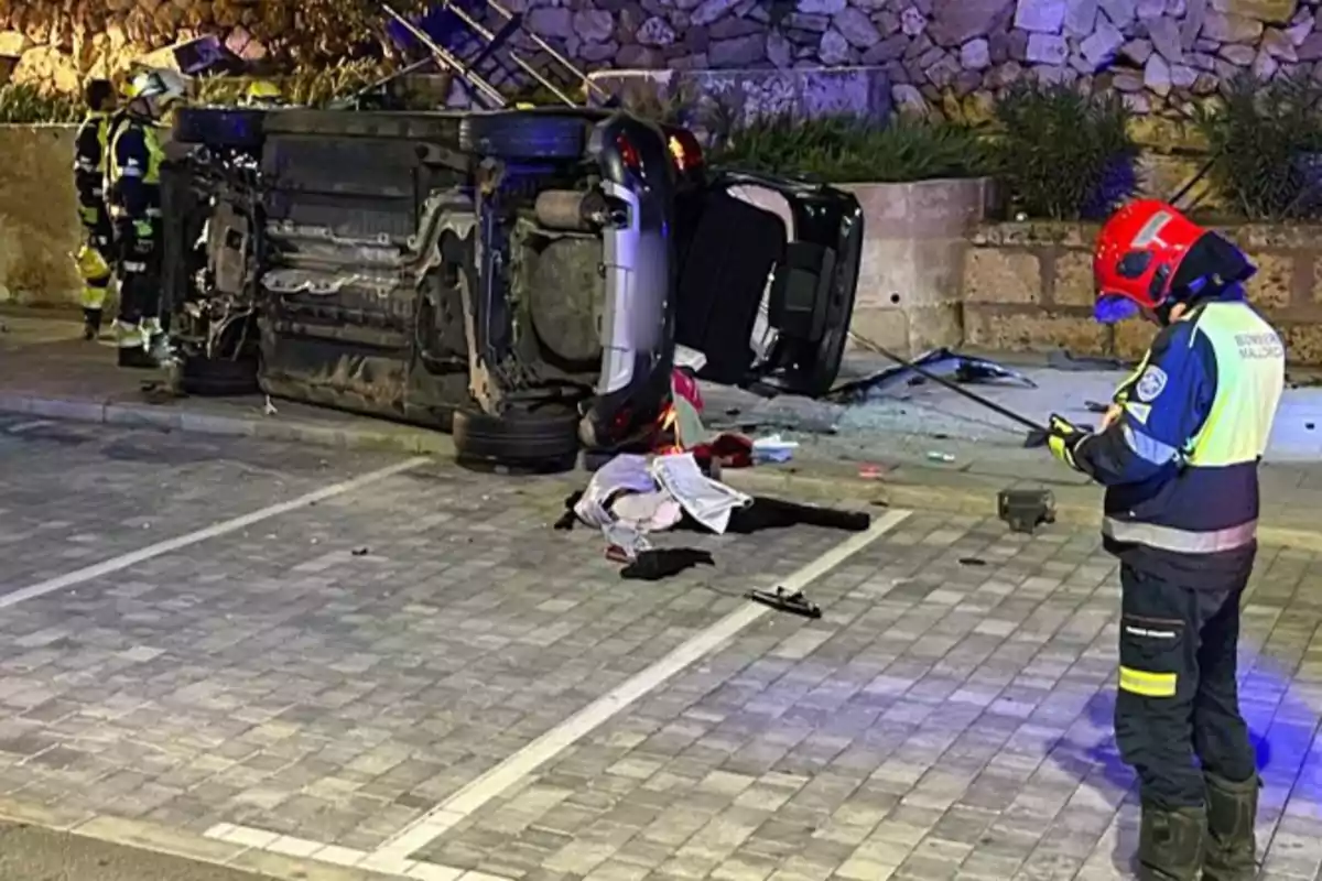 Un coche volcado en un estacionamiento con bomberos alrededor evaluando la escena.