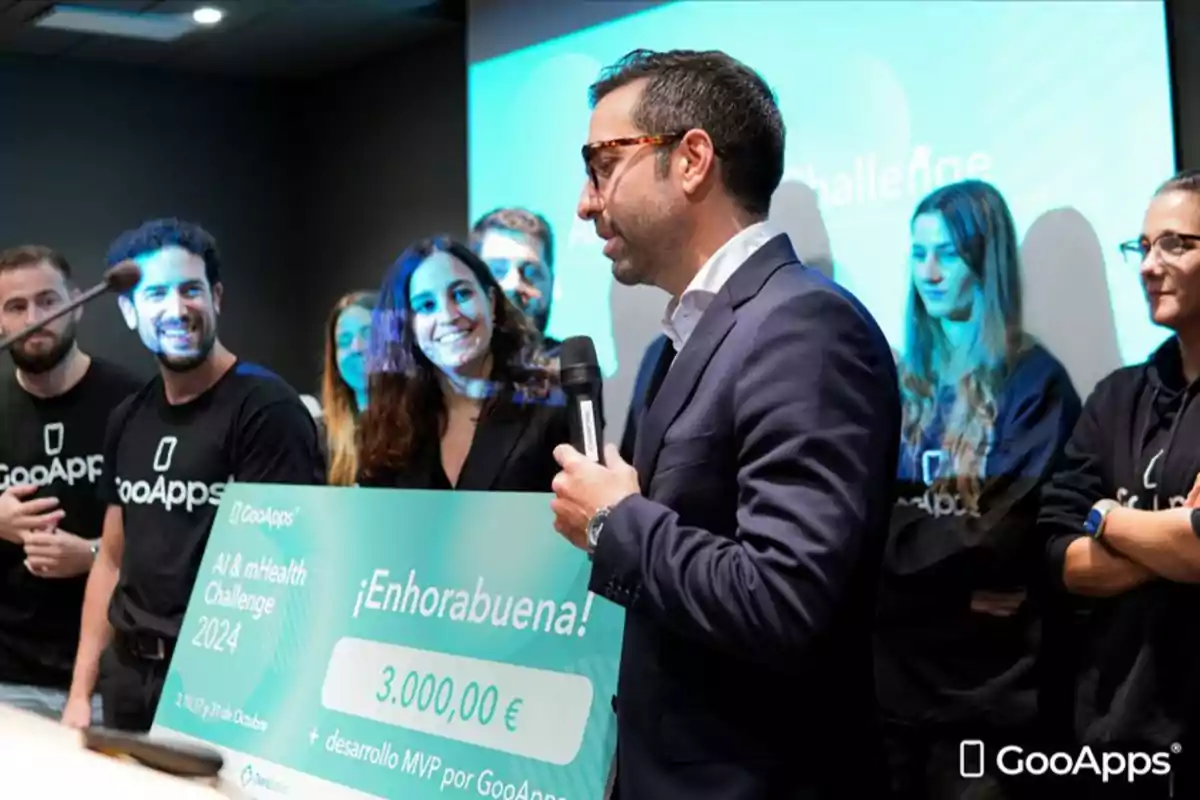 Un grupo de personas en un evento de GooApps, donde un hombre sostiene un micrófono y un cheque simbólico de 3000 euros.