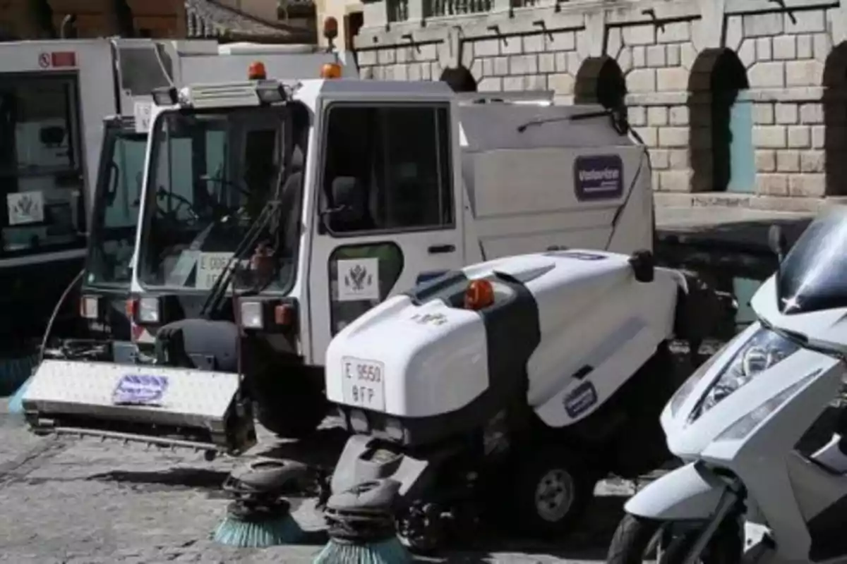 Vehículos de limpieza urbana estacionados en una calle empedrada frente a un edificio de piedra.