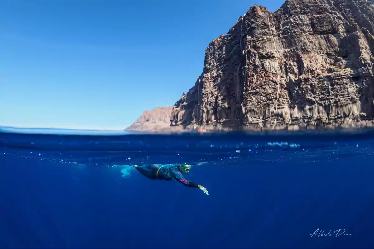 Persona buceando en aguas cristalinas cerca de un acantilado rocoso bajo un cielo despejado.