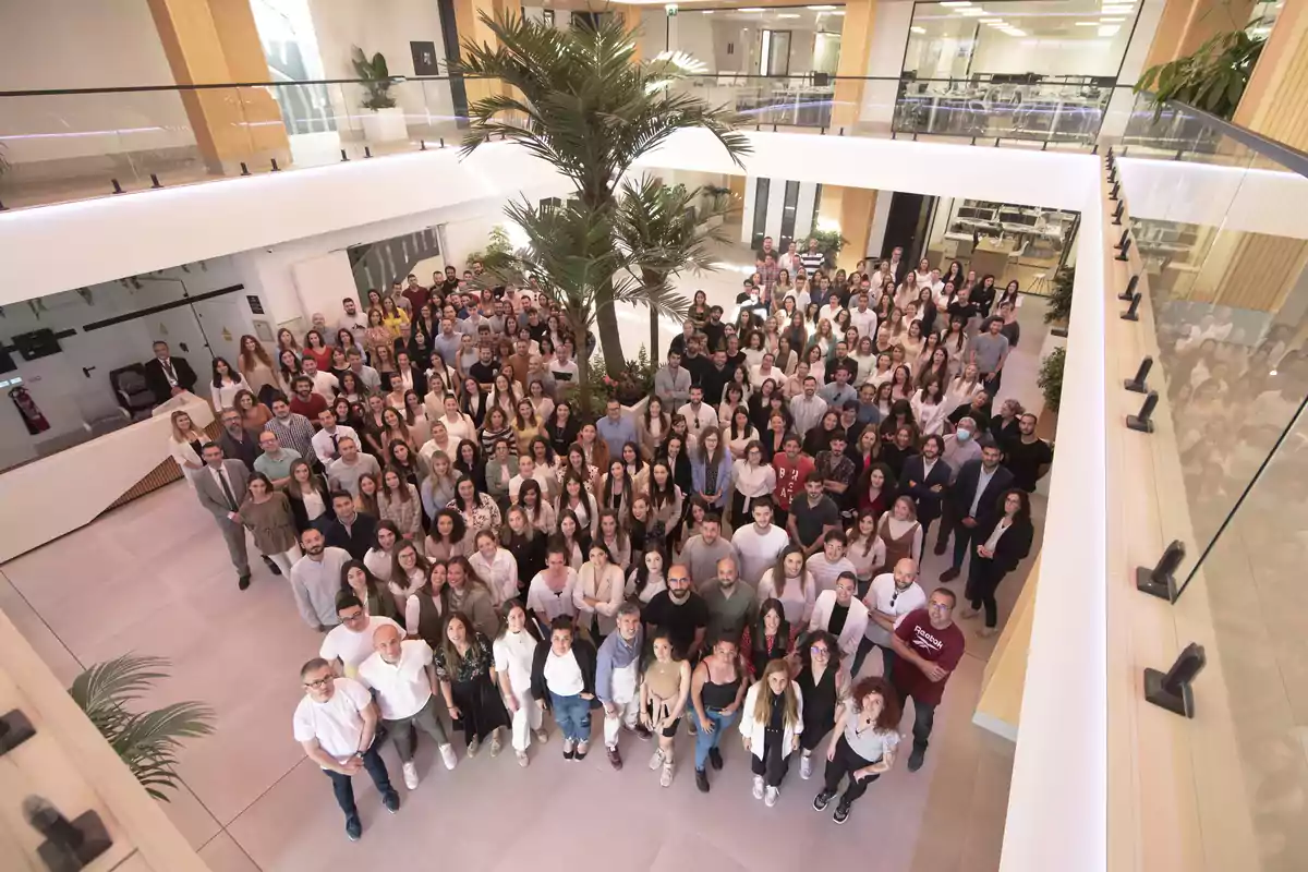 Un grupo grande de personas posando en el interior de un edificio moderno con una planta en el centro.