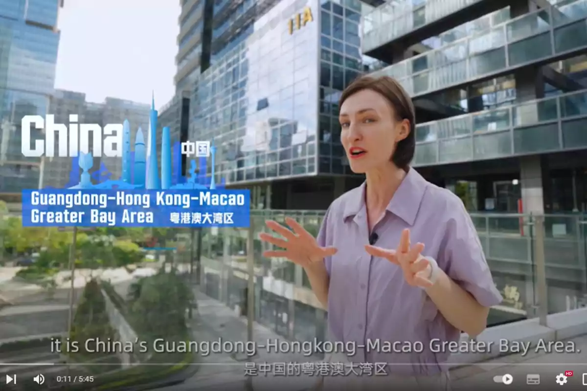 Una mujer está hablando frente a un edificio moderno con un cartel que dice "China Guangdong-Hong Kong-Macao Greater Bay Area".