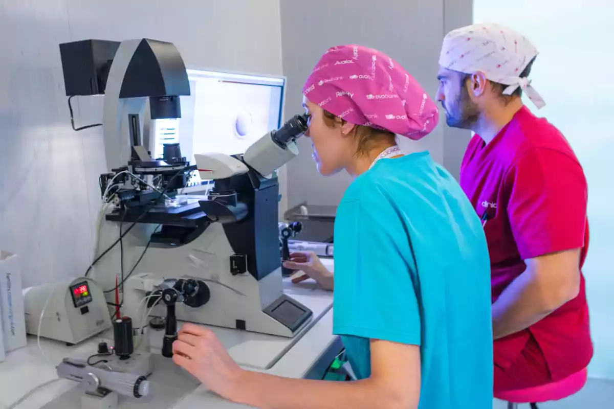 Dos personas con ropa médica observan a través de un microscopio en un laboratorio