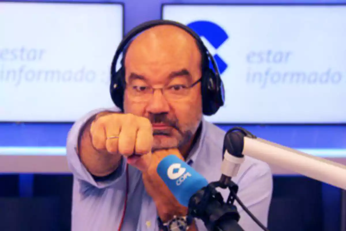 Hombre con auriculares y micrófono en un estudio de radio, apuntando con el puño hacia la cámara.