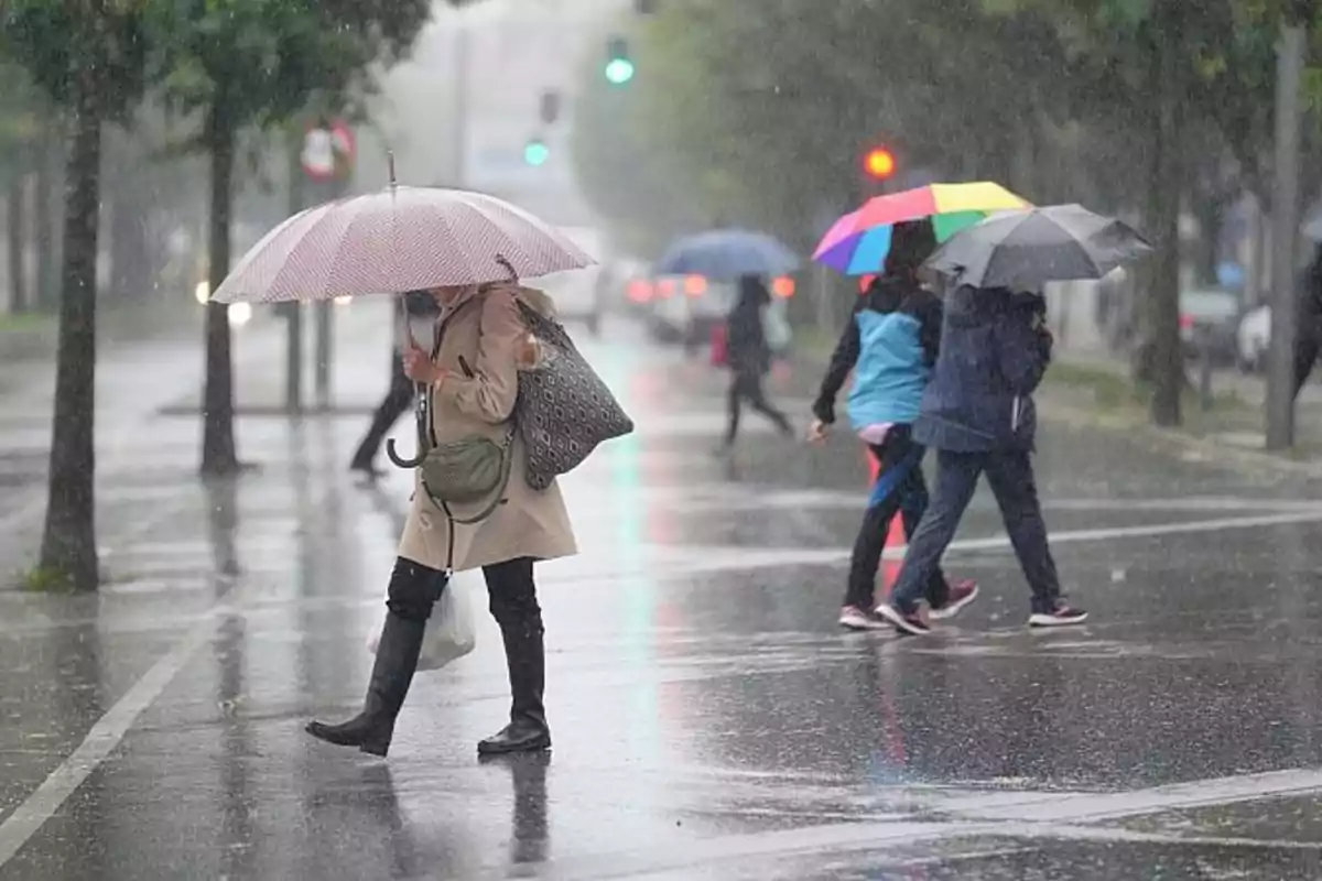 Personas caminando bajo la lluvia con paraguas en una calle urbana.