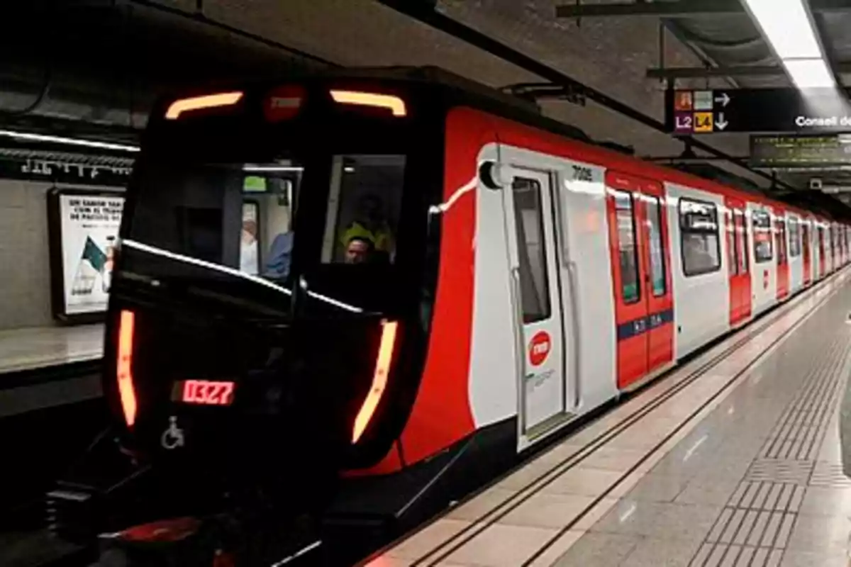 Un tren del metro rojo y blanco en una estación subterránea con señalización visible en el techo.