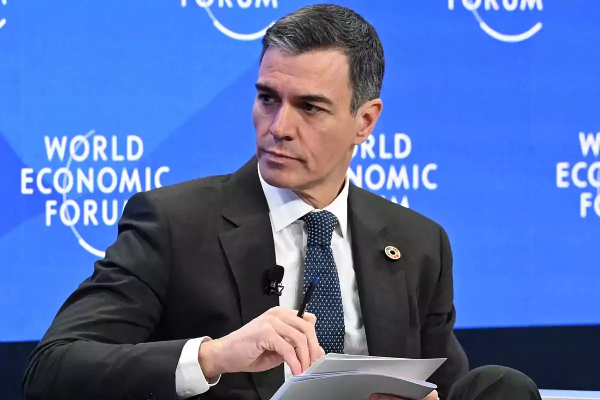 A man in a suit holding documents at a World Economic Forum event. A man in a suit holding documents at a World Economic Forum event.