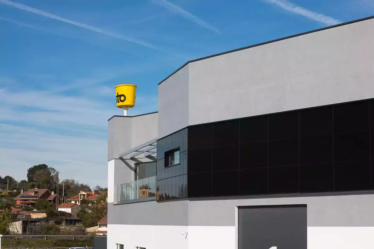 Edificio moderno con fachada gris y negra y un tanque amarillo en el techo bajo un cielo azul.