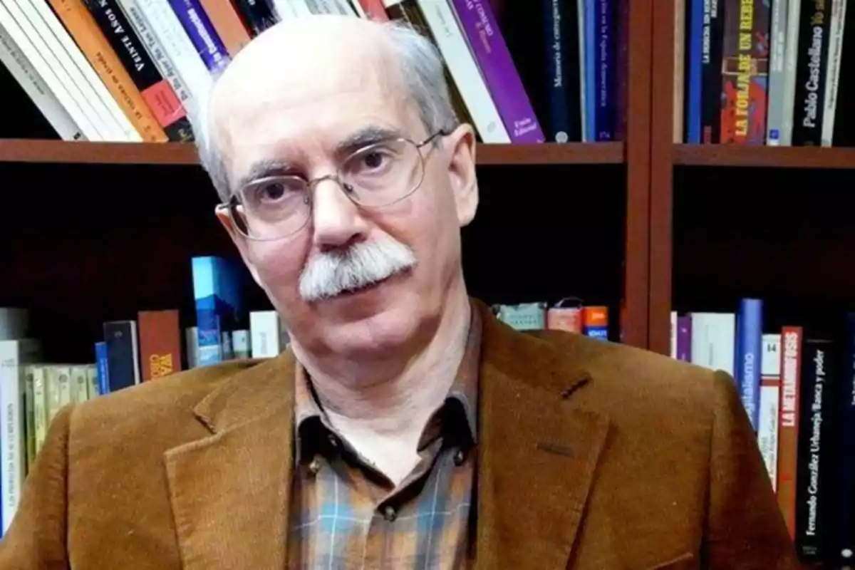 Un hombre con gafas y bigote está frente a una estantería llena de libros.