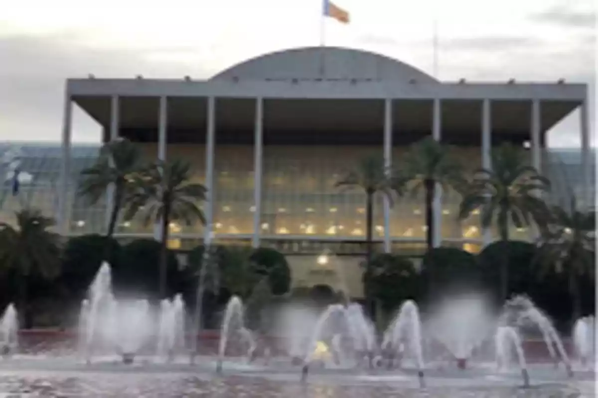 Modern building with columns and a fountain in the foreground surrounded by palm trees.