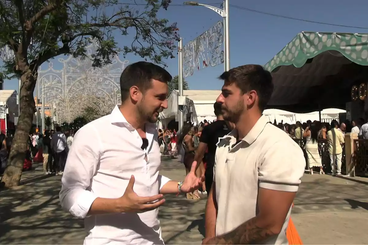 Dos hombres conversan en una feria al aire libre rodeados de gente y decoraciones festivas bajo un cielo despejado. Dos hombres conversan en una feria al aire libre rodeados de gente y decoraciones festivas bajo un cielo despejado.