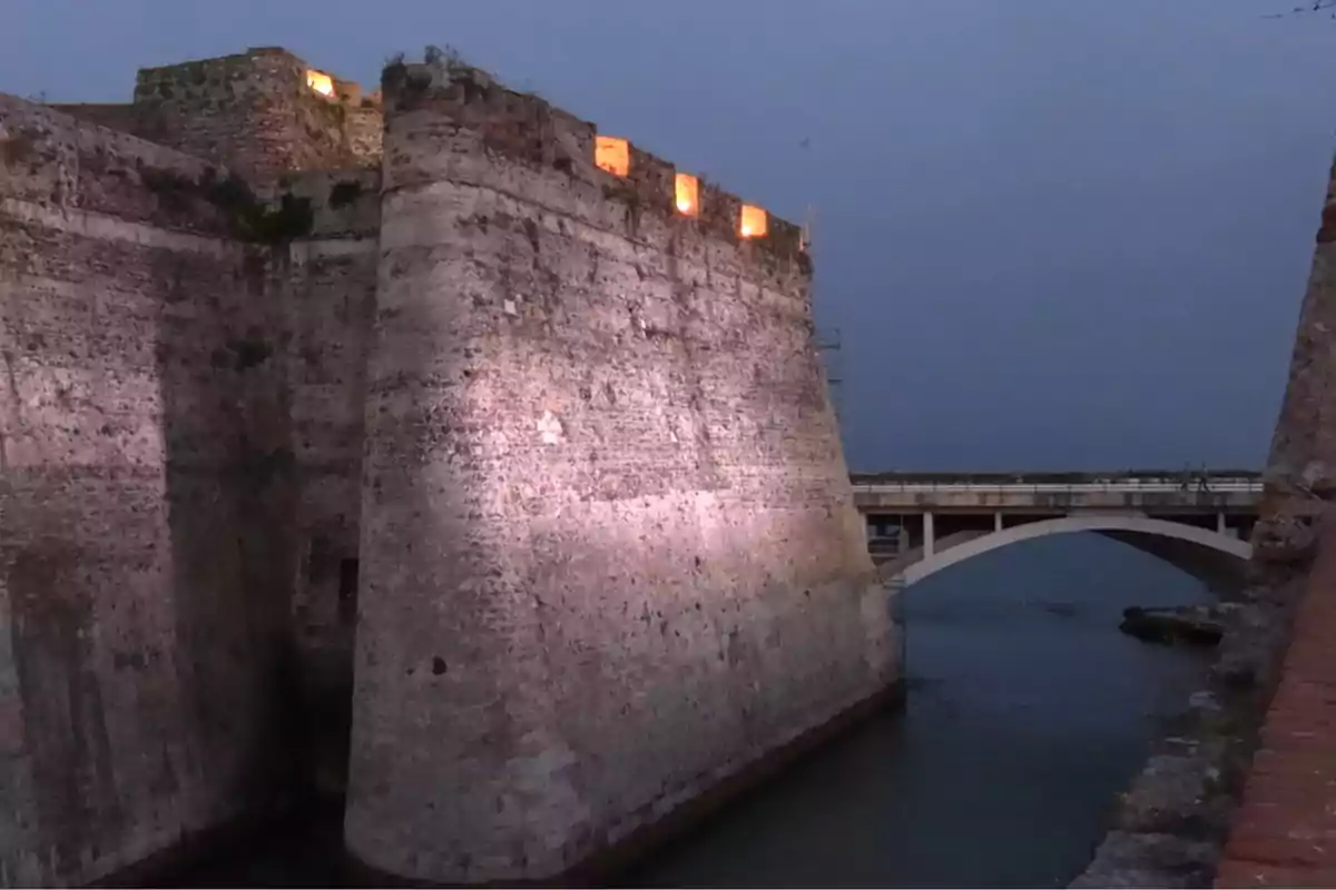 Murallas de piedra iluminadas al atardecer junto a un puente sobre el agua Murallas de piedra iluminadas al atardecer junto a un puente sobre el agua
