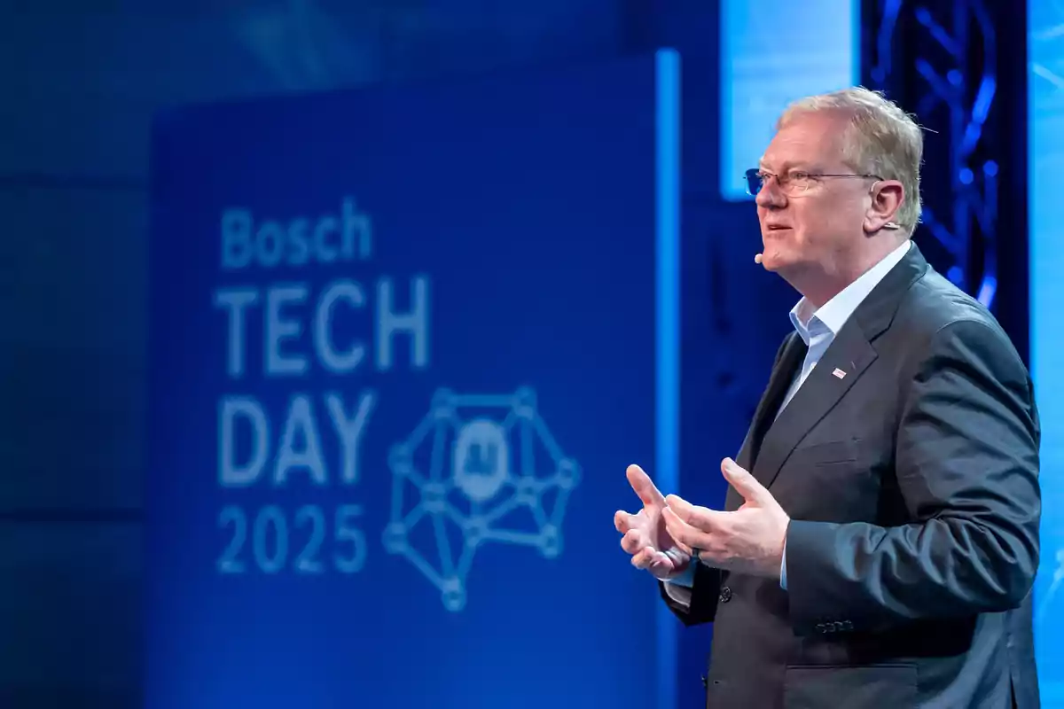 Hombre de traje hablando en un escenario durante el evento Bosch Tech Day 2025 con fondo azul y gráficos relacionados con inteligencia artificial.