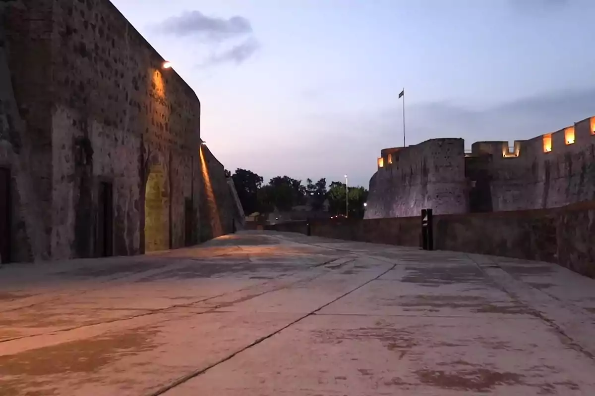 Fortaleza antigua con muros de piedra iluminados al atardecer y un camino amplio en primer plano Fortaleza antigua con muros de piedra iluminados al atardecer y un camino amplio en primer plano