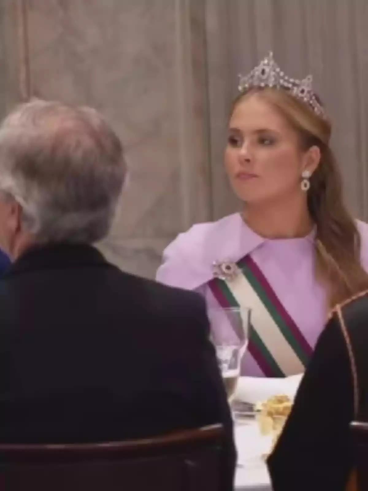 Woman with a tiara and ceremonial sash seated at an elegant table during a banquet