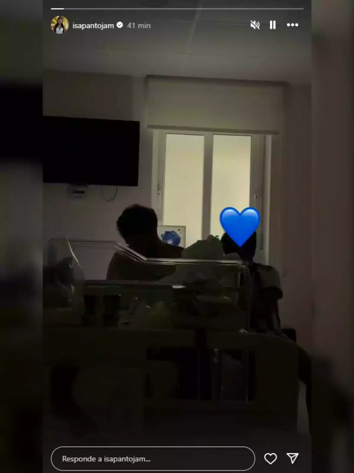 Habitación de hospital con dos personas sentadas junto a una cuna -una de ellas es Asraf Beno- y un corazón azul cubriendo el rostro de una de ellas. Habitación de hospital con dos personas sentadas junto a una cuna -una de ellas es Asraf Beno- y un corazón azul cubriendo el rostro de una de ellas.