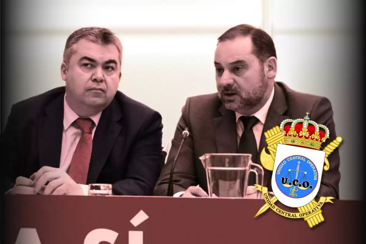 Dos hombres con traje y corbata sentados en una mesa durante una conferencia con un micrófono y una jarra de agua, junto a un escudo de la Unidad Central Operativa
