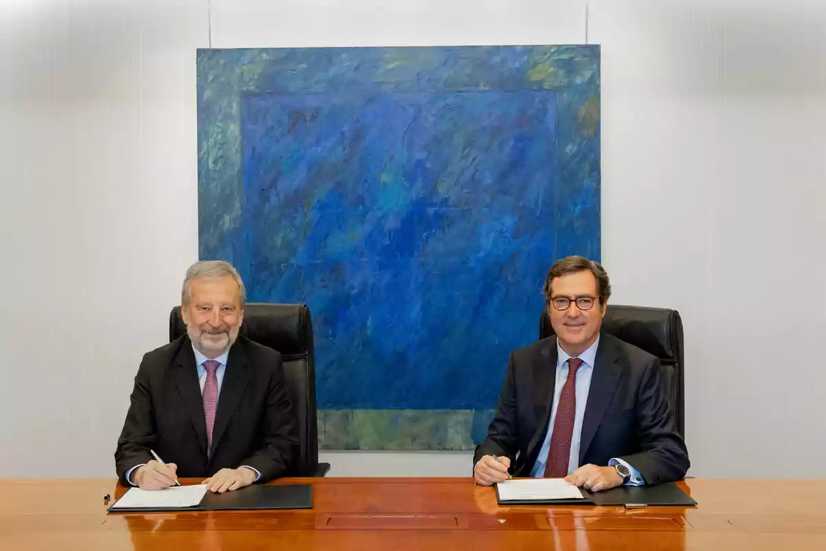 Dos hombres con traje y corbata sentados en una mesa de madera firmando documentos con una pintura abstracta azul de fondo Dos hombres con traje y corbata sentados en una mesa de madera firmando documentos con una pintura abstracta azul de fondo