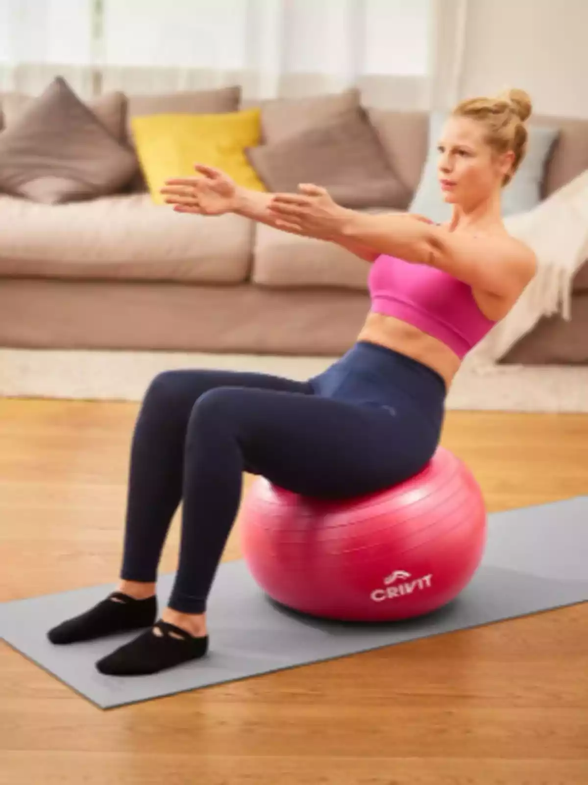 Mujer haciendo ejercicio sentada sobre una pelota de pilates rosa en una sala de estar Mujer haciendo ejercicio sentada sobre una pelota de pilates rosa en una sala de estar