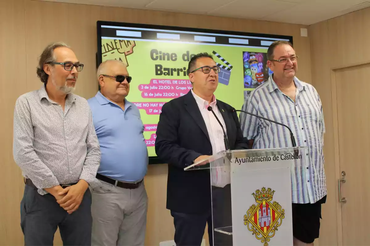 Cuatro hombres posan frente a un atril del Ayuntamiento de Castellón con una pantalla detrás que anuncia un ciclo de cine de barrio.