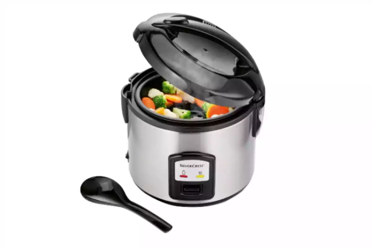 Olla arrocera eléctrica de acero inoxidable con tapa abierta y verduras en su interior junto a una cuchara negra Olla arrocera eléctrica de acero inoxidable con tapa abierta y verduras en su interior junto a una cuchara negra