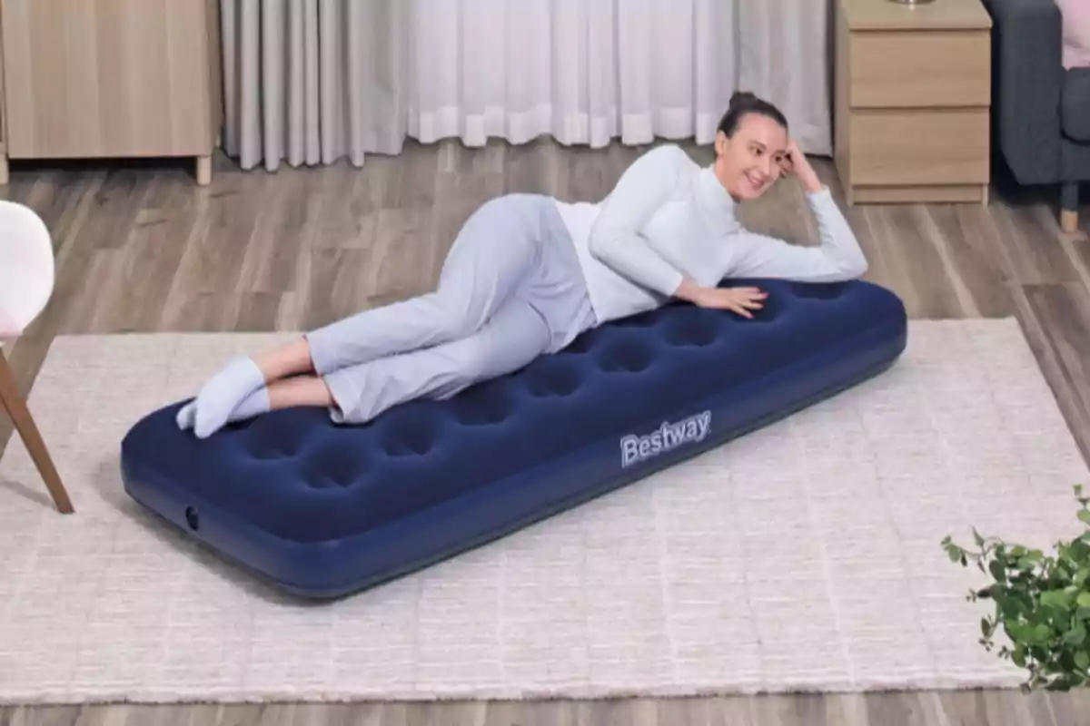 Mujer recostada sobre un colchón inflable azul en una habitación con piso de madera y alfombra clara Mujer recostada sobre un colchón inflable azul en una habitación con piso de madera y alfombra clara