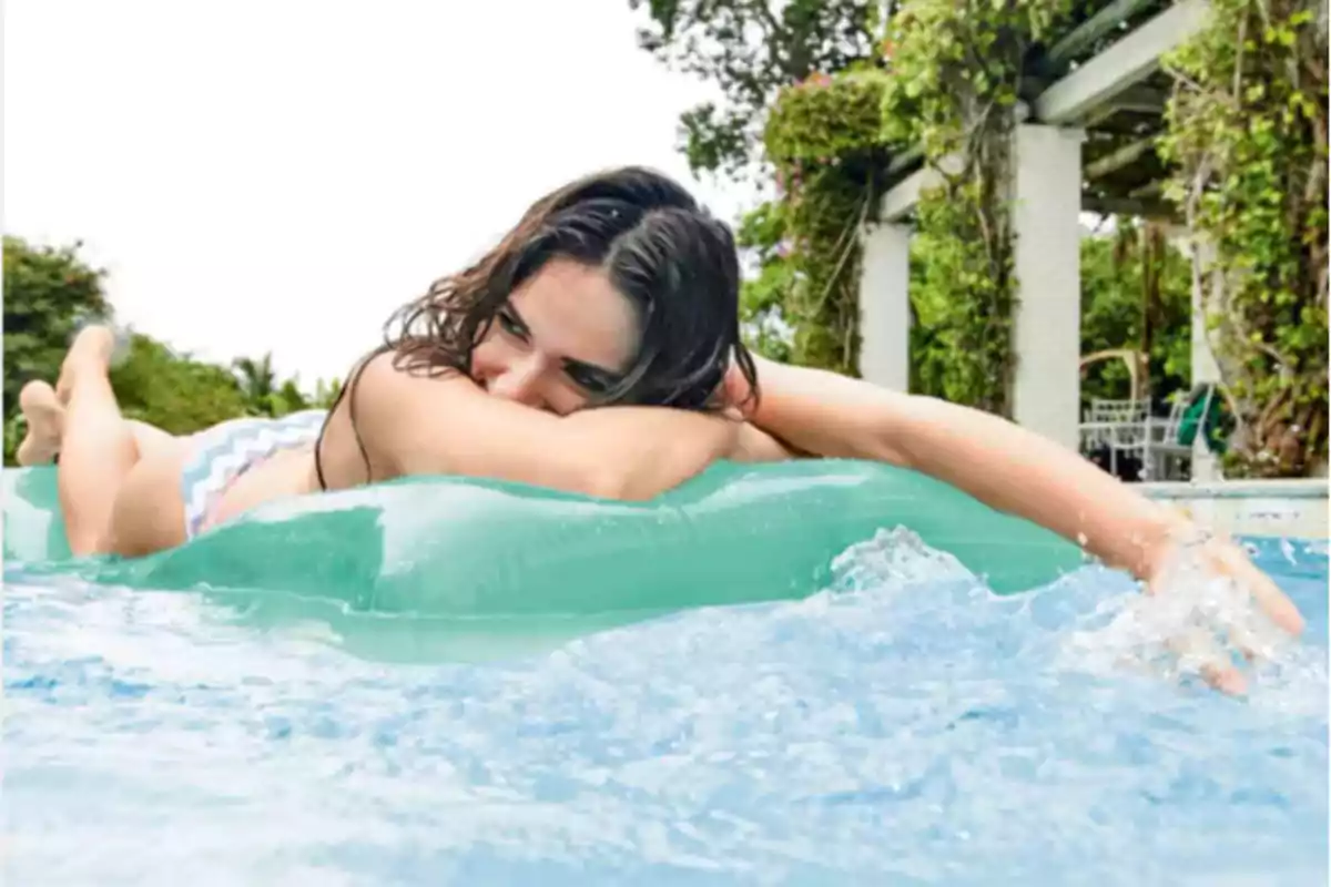 Mujer recostada sobre un inflable verde en una piscina disfrutando de un día soleado Mujer recostada sobre un inflable verde en una piscina disfrutando de un día soleado