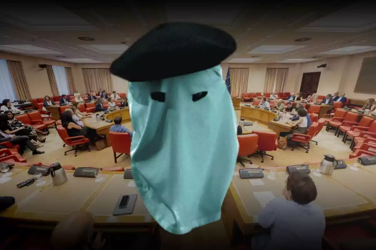 Persona con capucha y boina negra en primer plano dentro de una sala de reuniones con varias personas sentadas alrededor de una mesa redonda