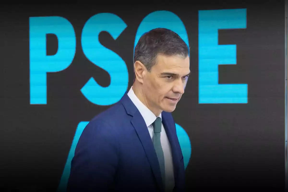 Hombre con traje azul y corbata verde frente a un fondo con las letras PSOE en grande