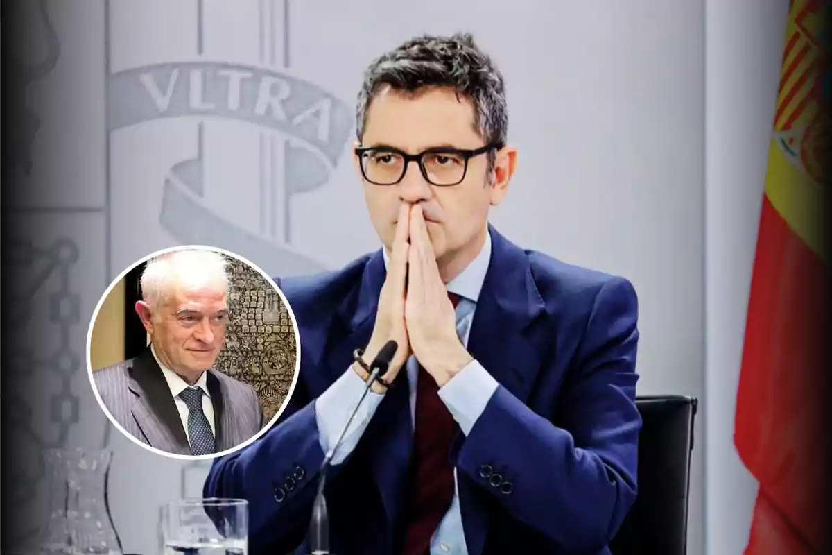 Hombre con gafas y traje azul sentado frente a un micrófono con las manos juntas en actitud pensativa y una bandera de España al fondo, con un recuadro circular que muestra a otro hombre mayor de cabello canoso y traje.