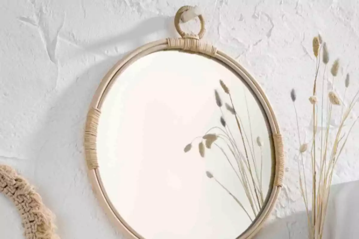 Espejo redondo con marco de mimbre colgado en una pared blanca reflejando ramas secas decorativas Espejo redondo con marco de mimbre colgado en una pared blanca reflejando ramas secas decorativas