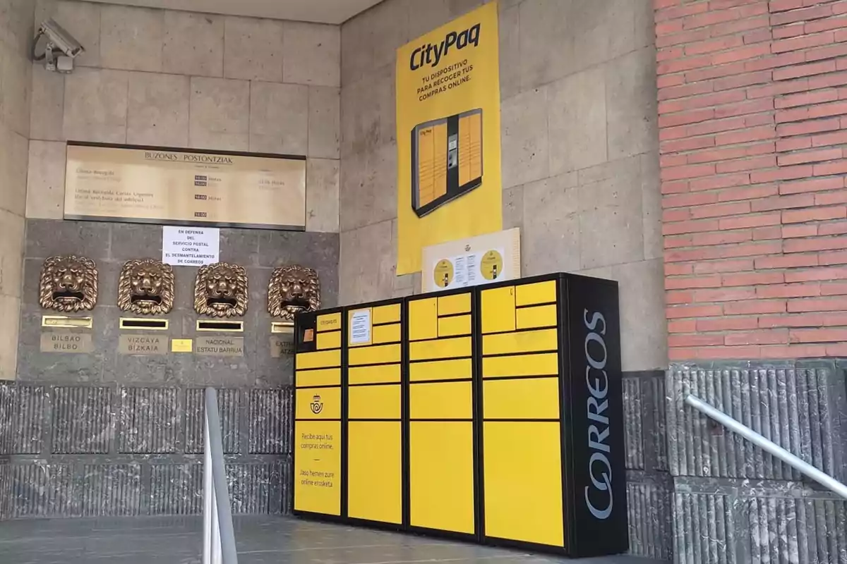 Buzones antiguos con forma de cabeza de león junto a un moderno casillero amarillo de paquetería de Correos en una oficina postal Buzones antiguos con forma de cabeza de león junto a un moderno casillero amarillo de paquetería de Correos en una oficina postal