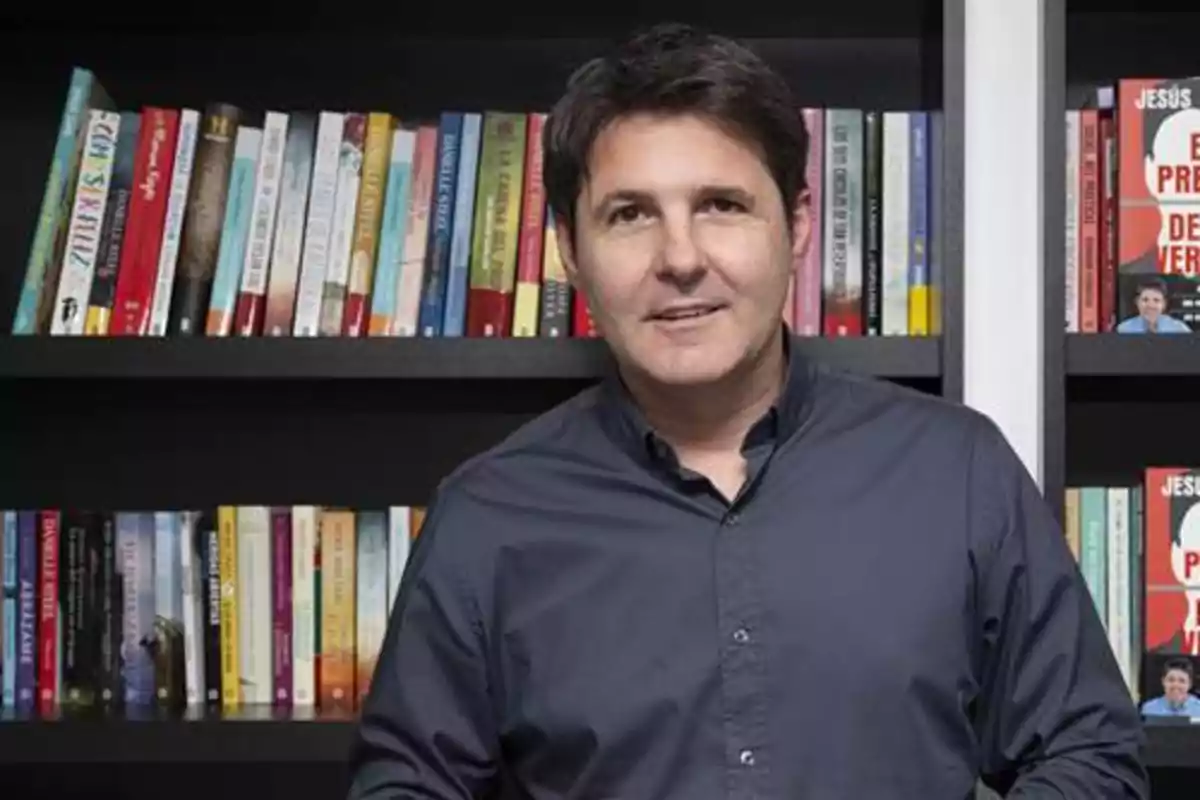 Hombre de cabello oscuro con camisa azul posando frente a una estantería llena de libros. Hombre de cabello oscuro con camisa azul posando frente a una estantería llena de libros.