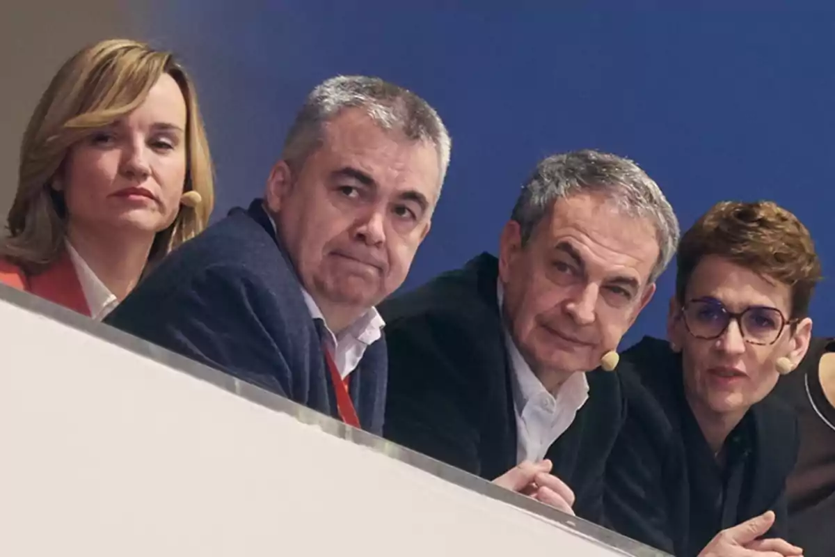 Cuatro personas sentadas en una mesa con micrófonos de diadema observando hacia el frente