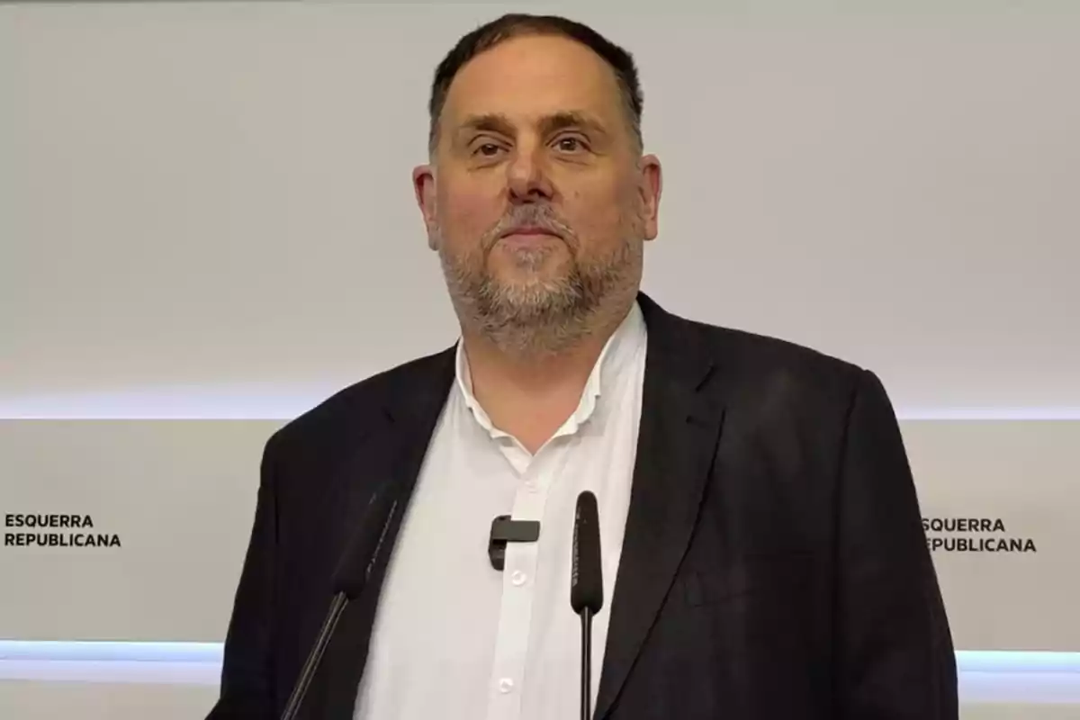 Hombre de mediana edad con barba y cabello corto, vestido con camisa blanca y chaqueta oscura, de pie frente a un atril con micrófonos y un fondo que dice Esquerra Republicana Hombre de mediana edad con barba y cabello corto, vestido con camisa blanca y chaqueta oscura, de pie frente a un atril con micrófonos y un fondo que dice Esquerra Republicana