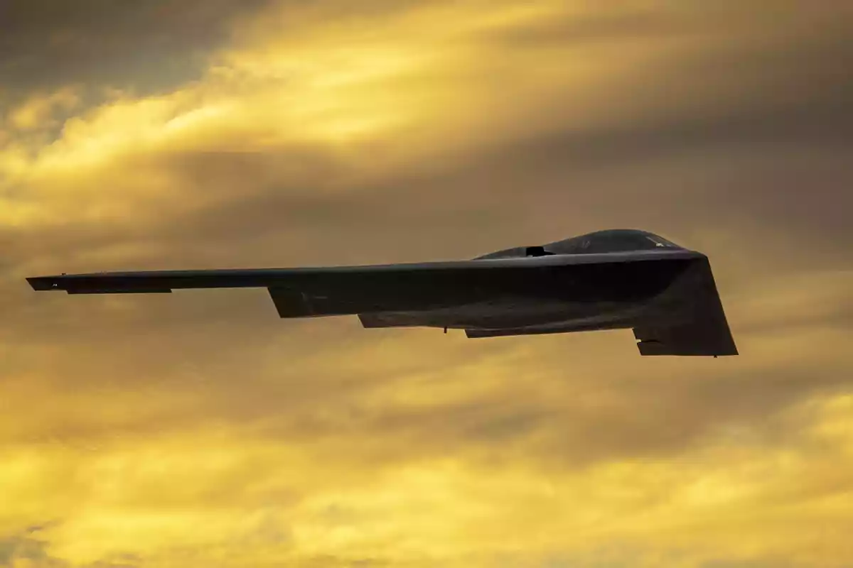 Avión bombardero furtivo volando frente a un cielo amarillo al atardecer