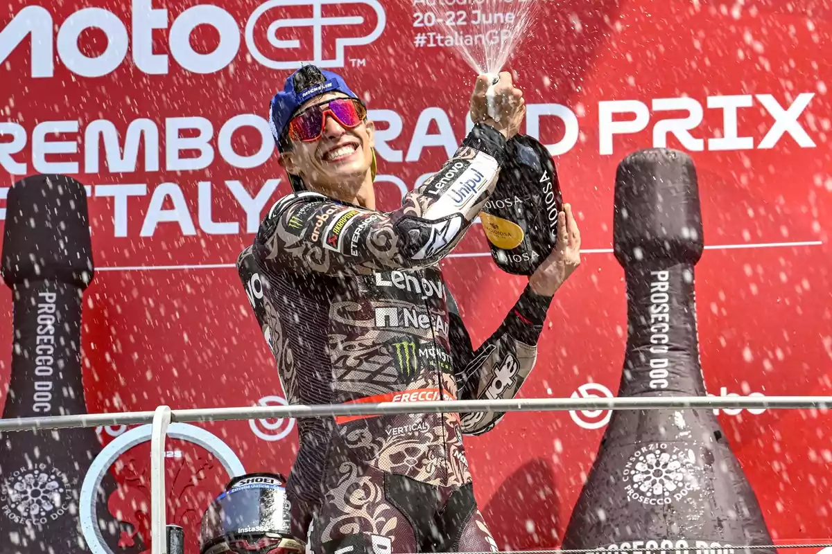 Piloto de motociclismo celebrando en el podio con una botella de champán mientras el líquido se esparce a su alrededor