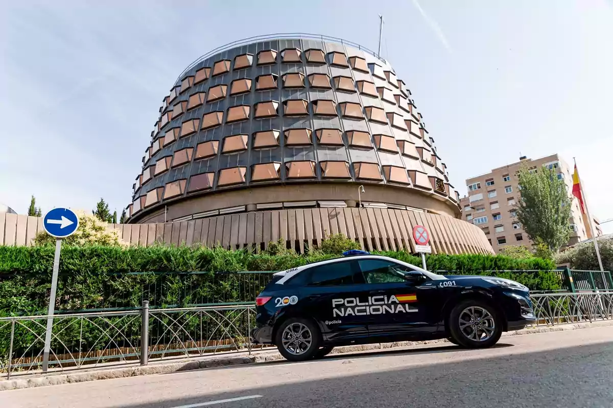 Edificio circular con ventanas geométricas y un coche de la Policía Nacional estacionado frente a una señal de dirección obligatoria a la derecha