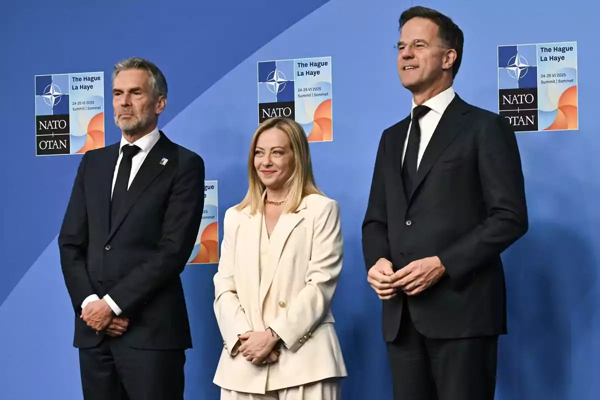 Tres personas vestidas de manera formal posan frente a un fondo azul con logotipos de la OTAN y el texto The Hague La Haye 24-25 VI 2025 Summit