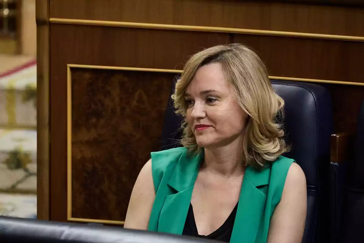 Mujer de cabello rubio y corto sentada en una silla azul con chaleco verde y fondo de madera Mujer de cabello rubio y corto sentada en una silla azul con chaleco verde y fondo de madera