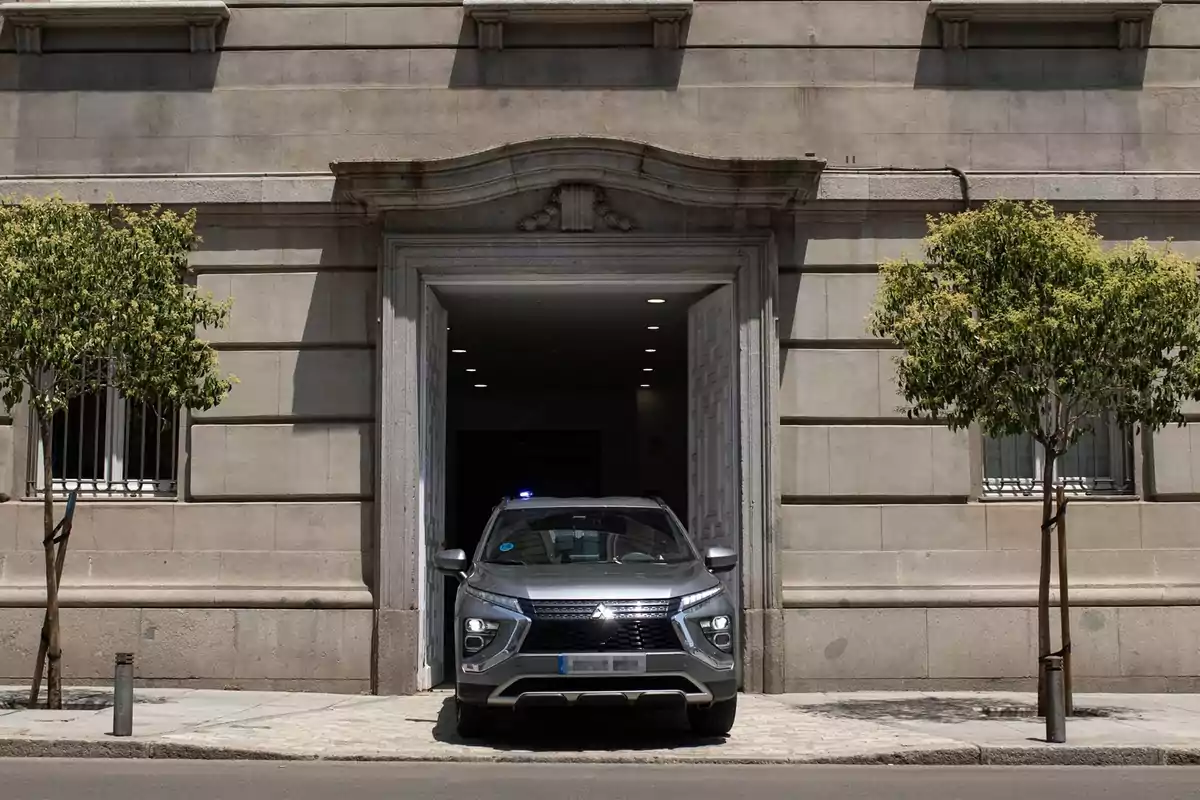 Un coche gris sale de un edificio antiguo entre dos árboles pequeños Un coche gris sale de un edificio antiguo entre dos árboles pequeños