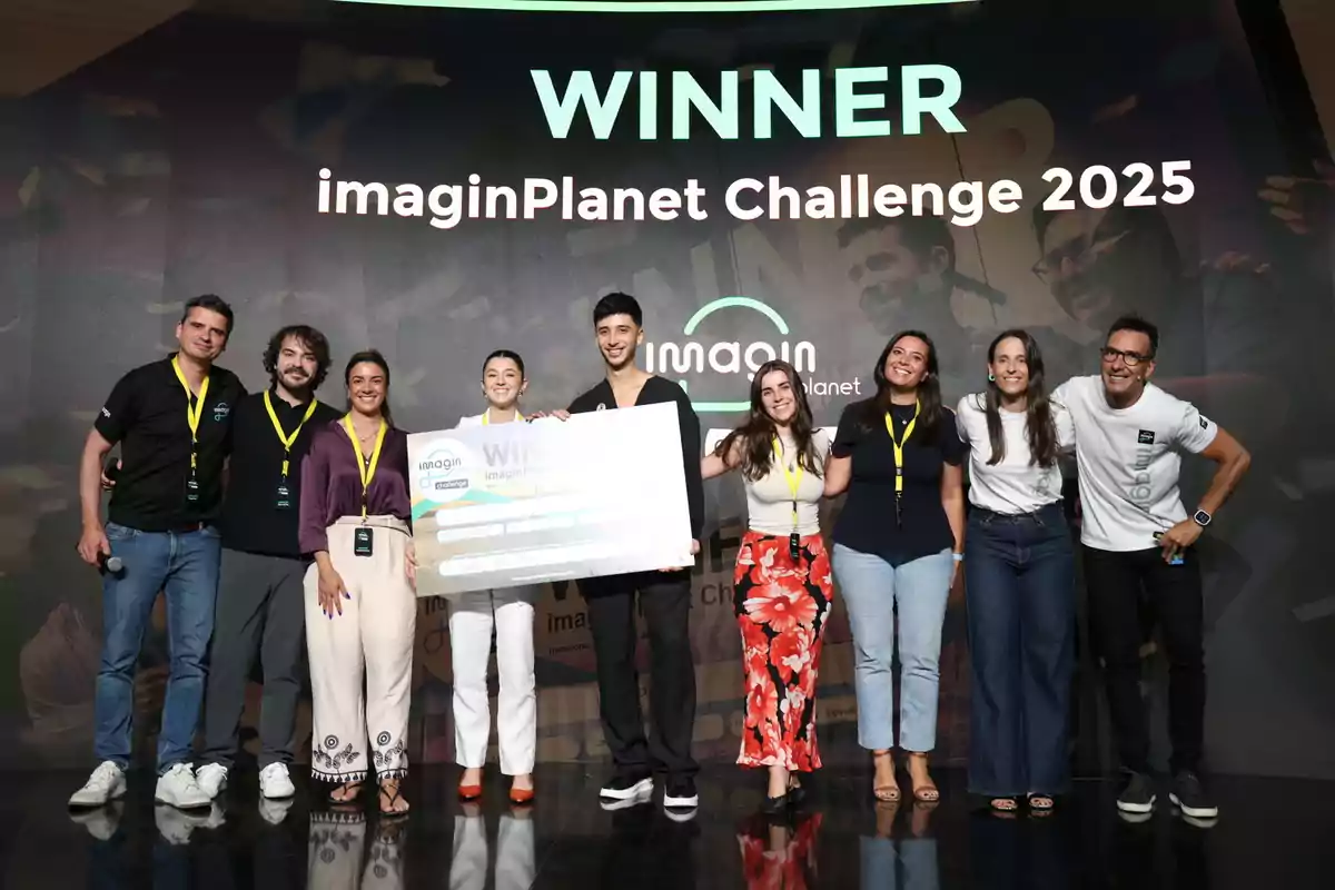 Grupo de personas sonrientes posando en el escenario con un cheque gigante como ganadores del imaginPlanet Challenge 2025 Grupo de personas sonrientes posando en el escenario con un cheque gigante como ganadores del imaginPlanet Challenge 2025