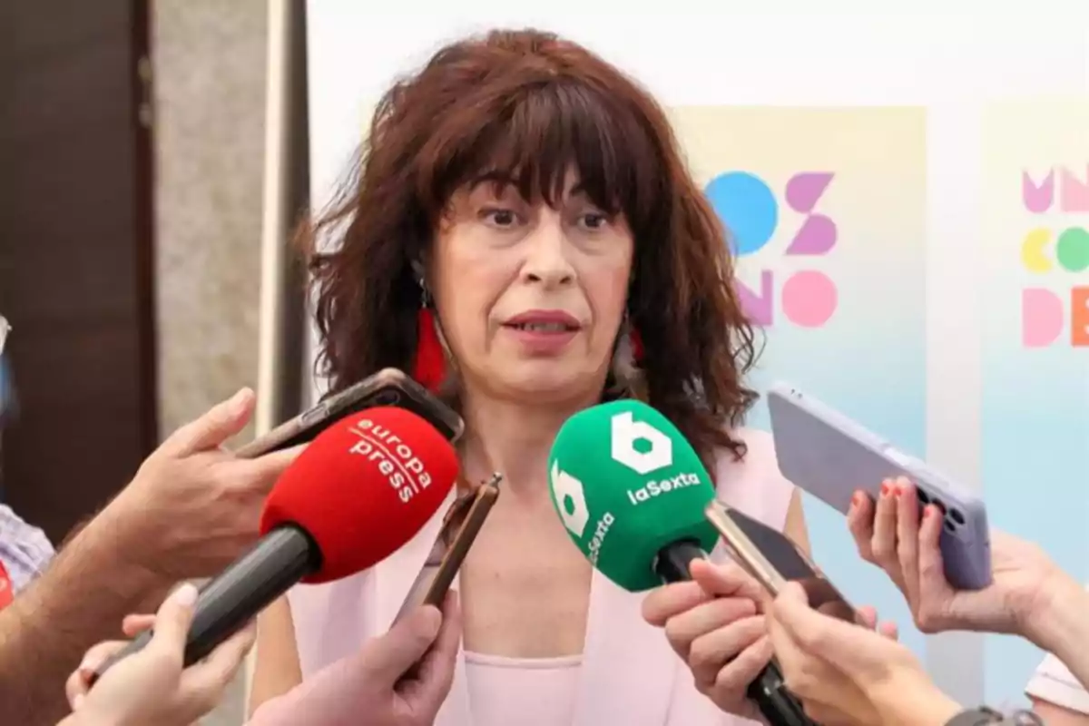 Mujer de cabello castaño y ondulado hablando ante varios micrófonos de diferentes medios de comunicación Mujer de cabello castaño y ondulado hablando ante varios micrófonos de diferentes medios de comunicación
