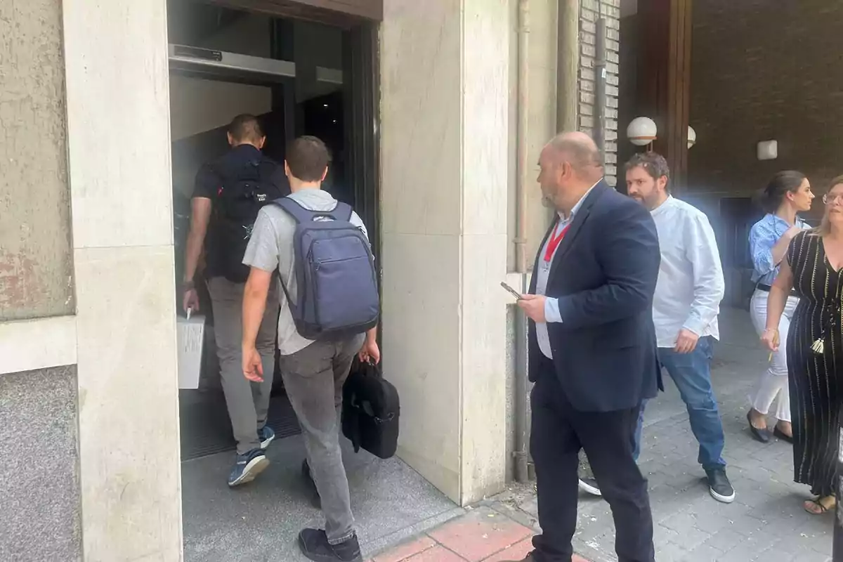 Varias personas entrando a un edificio por una puerta de entrada mientras otras caminan por la acera Varias personas entrando a un edificio por una puerta de entrada mientras otras caminan por la acera