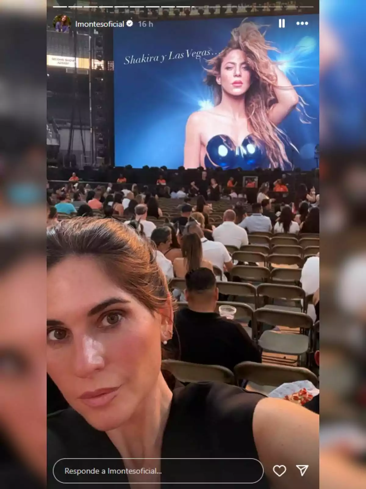 Lourdes Montes tomándose una selfie en un concierto con una pantalla gigante al fondo que muestra la imagen de una cantante famosa y el texto Shakira y Las Vegas, mientras el público espera sentado. Lourdes Montes tomándose una selfie en un concierto con una pantalla gigante al fondo que muestra la imagen de una cantante famosa y el texto Shakira y Las Vegas, mientras el público espera sentado.