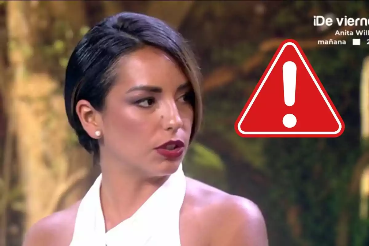 Anita Williams de cabello corto y oscuro con expresión seria, junto a un icono de advertencia rojo con un signo de exclamación blanco