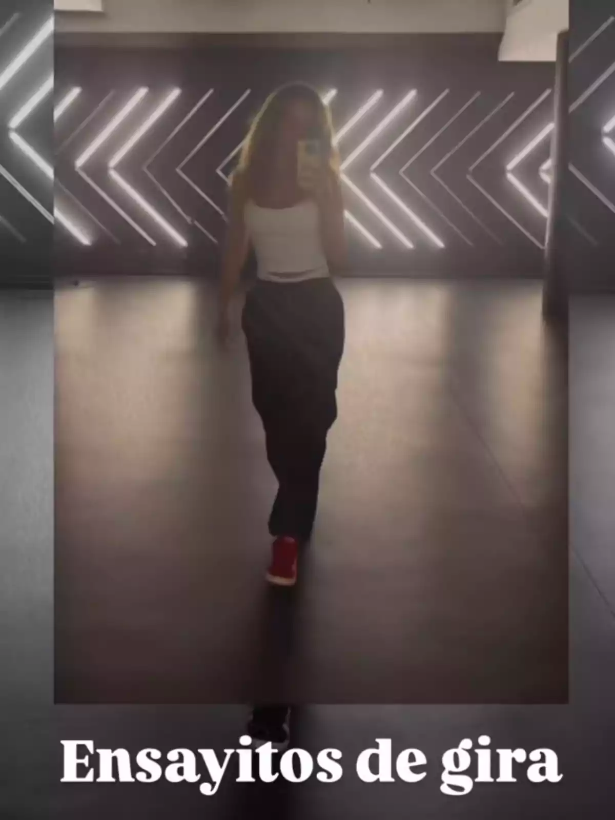Edurne tomándose una selfie frente a un espejo en un estudio de baile con luces en la pared y el texto Ensayitos de gira en la parte inferior Edurne tomándose una selfie frente a un espejo en un estudio de baile con luces en la pared y el texto Ensayitos de gira en la parte inferior